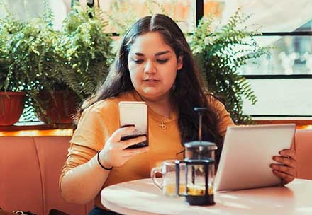 Girl on phone with tablet at cafe.