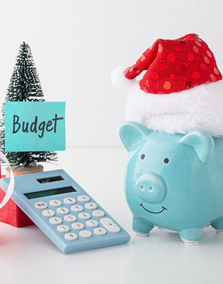 piggy bank with Santa Claus hat next to a calculator and a miniature tree with a sticky note that says "Budget"