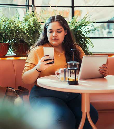 Girl on phone with tablet at cafe.