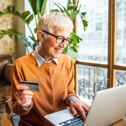 mature woman holding a card and looking at a laptop